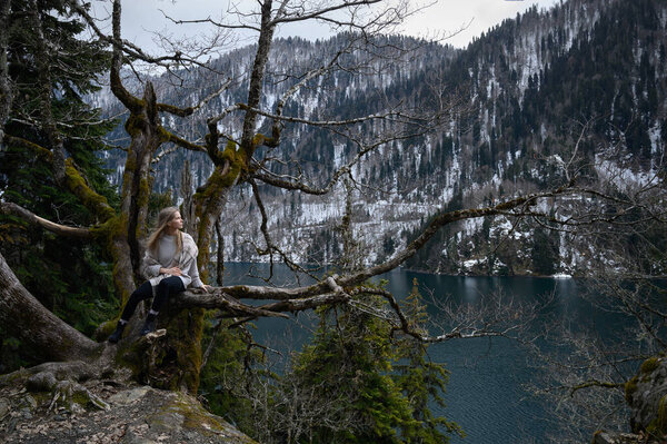 Girl sits on a tree and meditates near lake Ritsa in Abkhazia