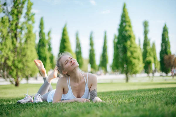 Atrakcyjna sportowa dziewczyna leży na trawie i relaksuje się w parku — Zdjęcie stockowe