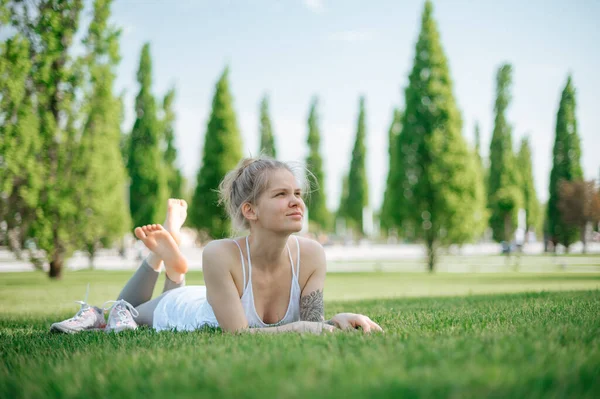 Aantrekkelijk sportief meisje ligt op het gras en ontspant in het park — Stockfoto