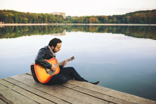 Young man playing on guitar at the lake — Stock Photo, Image