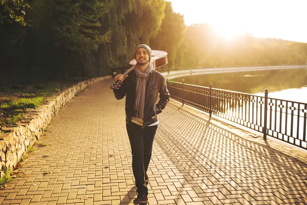 Young man walks by the lake and holding guitar — Stock Photo, Image