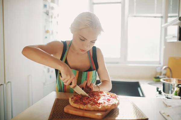 Jonge vrouw met een mes snijden de pizza — Stockfoto