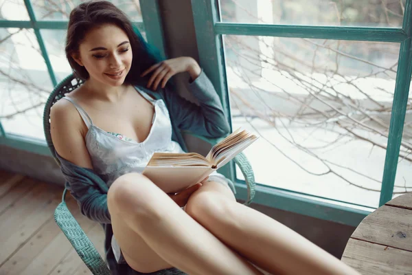 Ung kvinna läser boken sitter nära fönster — Stockfoto