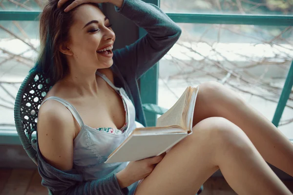 Молодая женщина читает книгу сидя у окна — стоковое фото