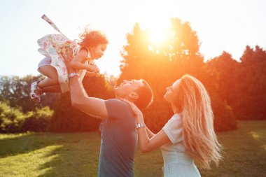 Mutlu genç aile dışarıda yeşil doğada birlikte vakit geçiriyor..