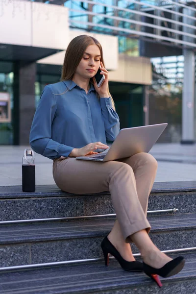 Mulher falando no celular e trabalhando com seu laptop enquanto está sentado nos passos — Fotografia de Stock