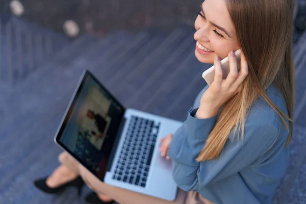 Mulher falando no celular e trabalhando com seu laptop enquanto está sentado nos passos — Fotografia de Stock