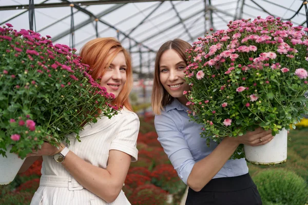 Usmívající se ženy pózující s květinami ve skleníku — Stock fotografie