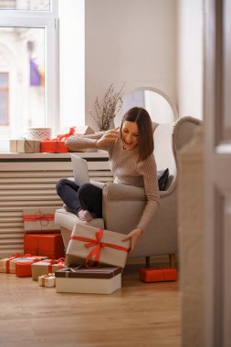 Evdeki koltukta oturan bir kadın dizüstü bilgisayarla çalışıyor, cep telefonuyla konuşuyor.