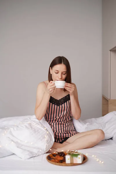 Egy nő kávét iszik az ágyban ajándékokkal. — Stock Fotó