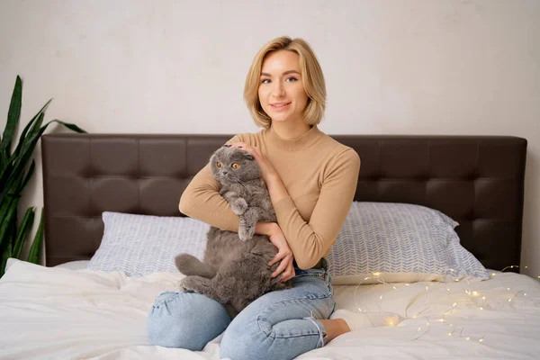 Молодая женщина и кошка на кровати в комнате — стоковое фото