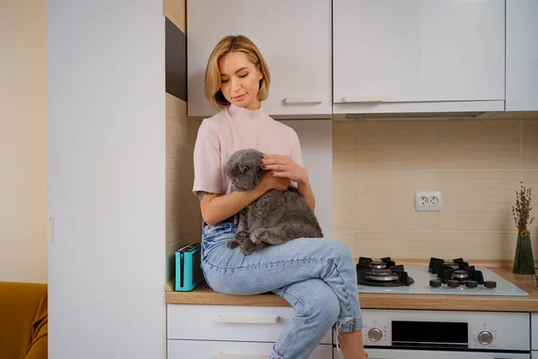 Женщина, сидящая на кухне и обнимающая кота — стоковое фото