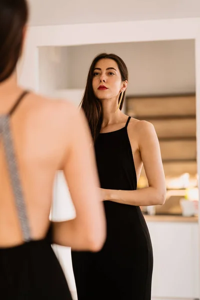 Señora lleva hermoso vestido negro mirando en el espejo — Foto de Stock