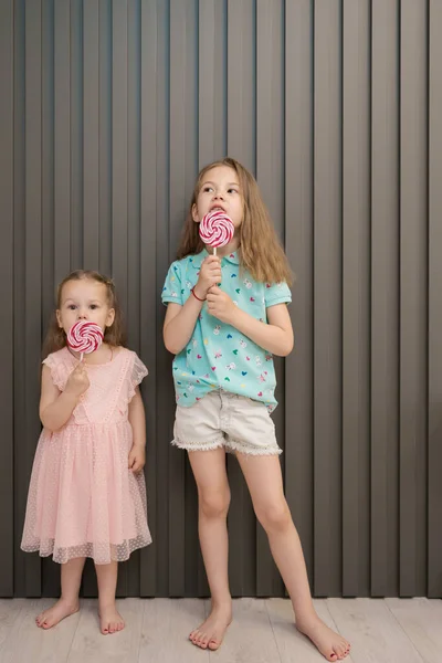 Милые маленькие девочки с леденцом на сером фоне — стоковое фото