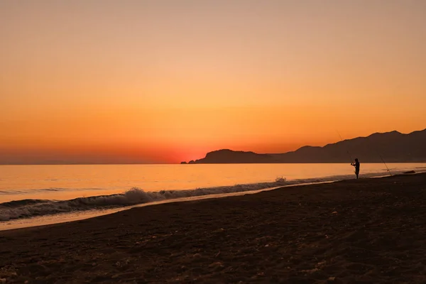 Человек рыбачит в море на восходе солнца — стоковое фото