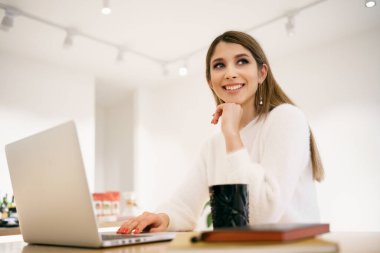 Kafede dizüstü bilgisayar kullanan ve latte içen genç bir kadın.