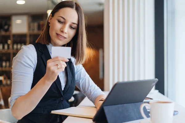 Mujer sonriente sosteniendo una tarjeta mientras usa la tableta — Foto de Stock