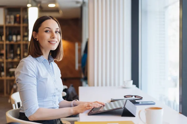 Portret van een jonge vrouw die koffie drinkt aan tafel met tablet in café — Stockfoto