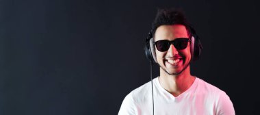 Kaygısız koyu tenli adam portresi siyah arka planda kulaklık takıyor.