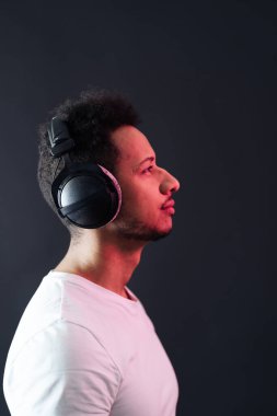 Kaygısız koyu tenli adam portresi siyah arka planda kulaklık takıyor.