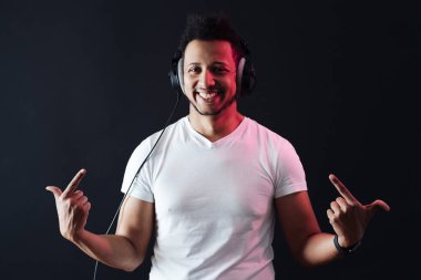 Kaygısız koyu tenli adam portresi siyah arka planda kulaklık takıyor.