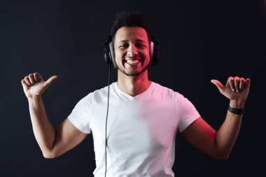 Kaygısız koyu tenli adam portresi siyah arka planda kulaklık takıyor.