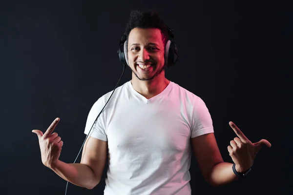 Carefree dark skinned guy portrait wearing headphones on black background — Stock Photo, Image