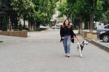 Yürüyen, tartışan ve şehirdeki dalmaçyalı evcil hayvanıyla oynayan bir kadın.
