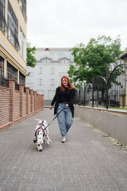 Yürüyen, tartışan ve şehirdeki dalmaçyalı evcil hayvanıyla oynayan bir kadın.