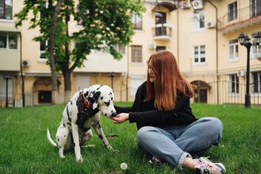 Güzel bir kadın sokak arka planında Dalmaçyalı köpeğe poz veriyor ve sarılıyor.