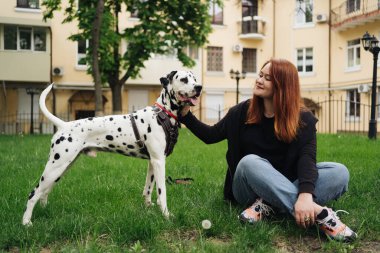 Güzel bir kadın sokak arka planında Dalmaçyalı köpeğe poz veriyor ve sarılıyor.