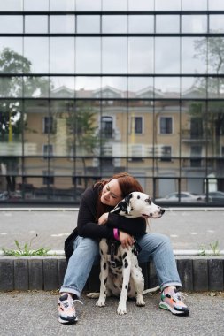 Güzel bir kadın sokak arka planında Dalmaçyalı köpeğe poz veriyor ve sarılıyor.