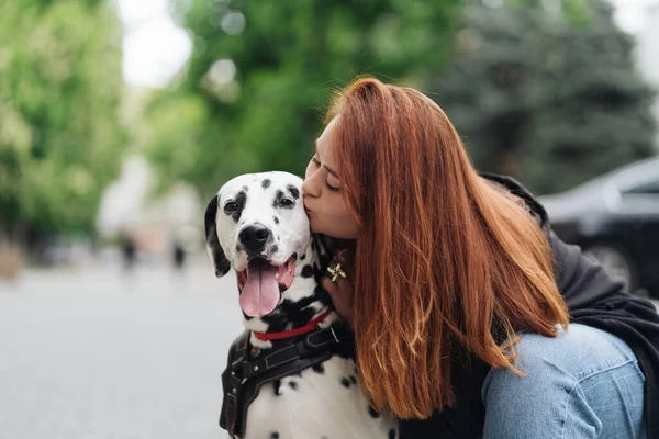 Pretty woman kissing dalmatian dog on street city background — Stock Photo, Image