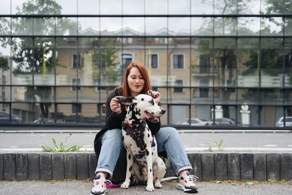 Ładna kobieta pozowanie i przytulanie dalmatyński pies na ulicy tło miasta — Zdjęcie stockowe