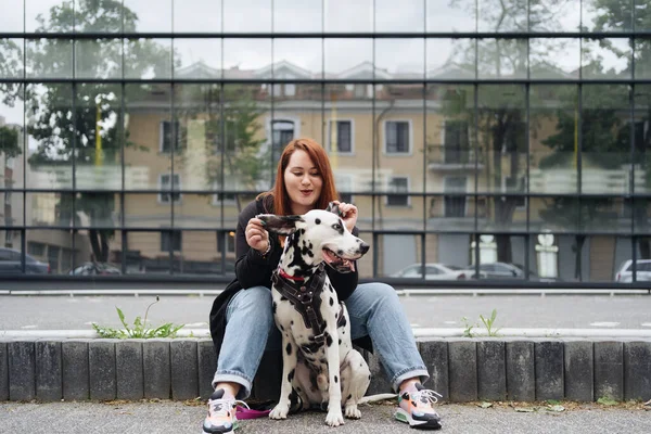 Güzel bir kadın sokak arka planında Dalmaçyalı köpeğe poz veriyor ve sarılıyor.