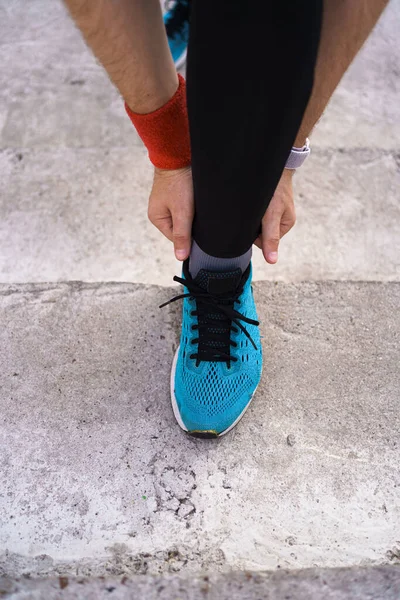 Человек завязывает свою спортивную обувь на бетонном фоне — стоковое фото