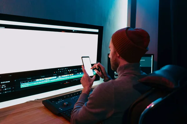 Muž Video Editor sedí ve svém počítači pomocí telefonu prázdné obrazovky — Stock fotografie