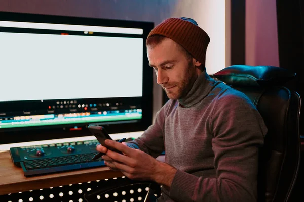 Muž Video Editor sedí ve svém počítači pomocí telefonu — Stock fotografie