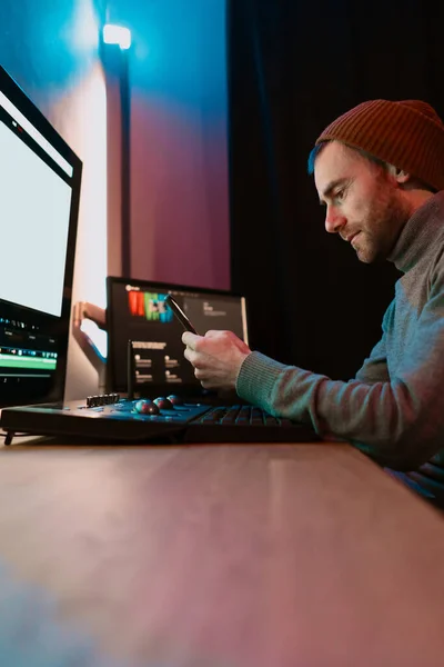 Mężczyzna wideo edytor siedzi przy jego komputer za pomocą telefon pusty ekran — Zdjęcie stockowe