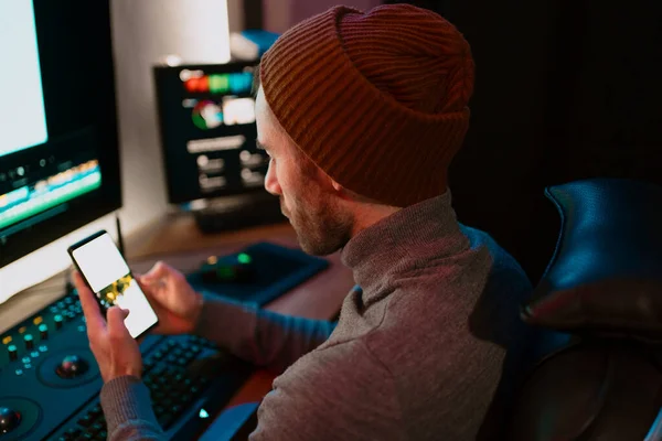 Editor de Vídeo Masculino sentado em seu computador usando tela em branco do telefone — Fotografia de Stock