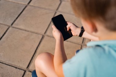 Okullu çocuk merdivenlerde otururken akıllı telefon kullanıyor.