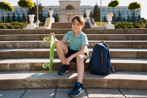 Boy sitting on the stairs with a backpack and penny — Stock Photo, Image