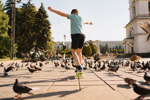 Un niño montando un patín en el parque con palomas — Foto de Stock