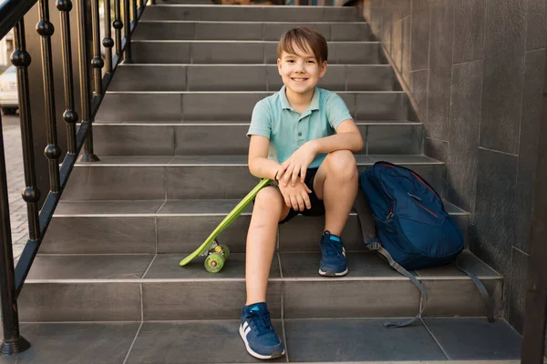 Chłopiec siedzi na schodach z plecakiem i monetą — Zdjęcie stockowe
