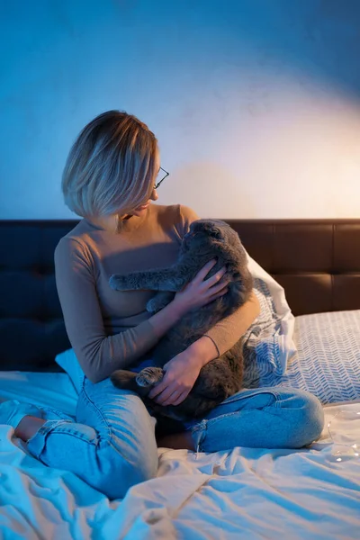 Mladá žena a kočka na posteli v pokoji — Stock fotografie