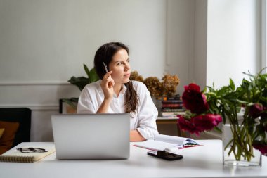 İş kadını dizüstü bilgisayarla çalışıyor evde oturuyor ve işlerini ev ofisinden yönetiyor.