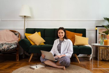 İş kadını dizüstü bilgisayarla çalışıyor evde oturuyor ve işlerini ev ofisinden yönetiyor.