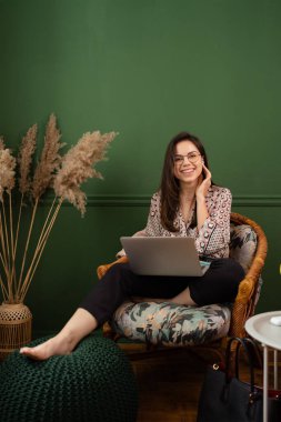 İş kadını dizüstü bilgisayarla çalışıyor evde oturuyor ve işlerini ev ofisinden yönetiyor.