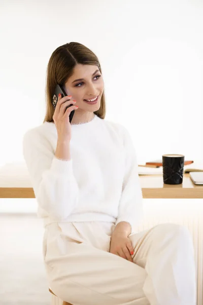Mulher sorridente falando no smartphone bebendo café dentro de casa — Fotografia de Stock