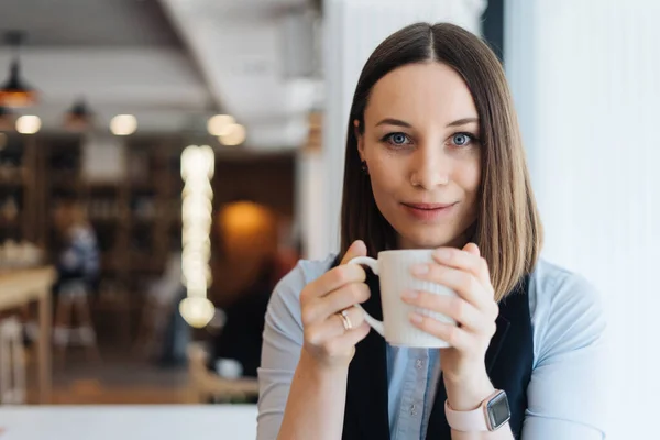 Portret van een jonge vrouw die koffie drinkt aan tafel in café — Stockfoto